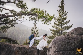 In South Lake Tahoe, California, a wedding photographer captures a serene image on a foggy day. The image shows the couple carefully walking among boulders under pine branches.